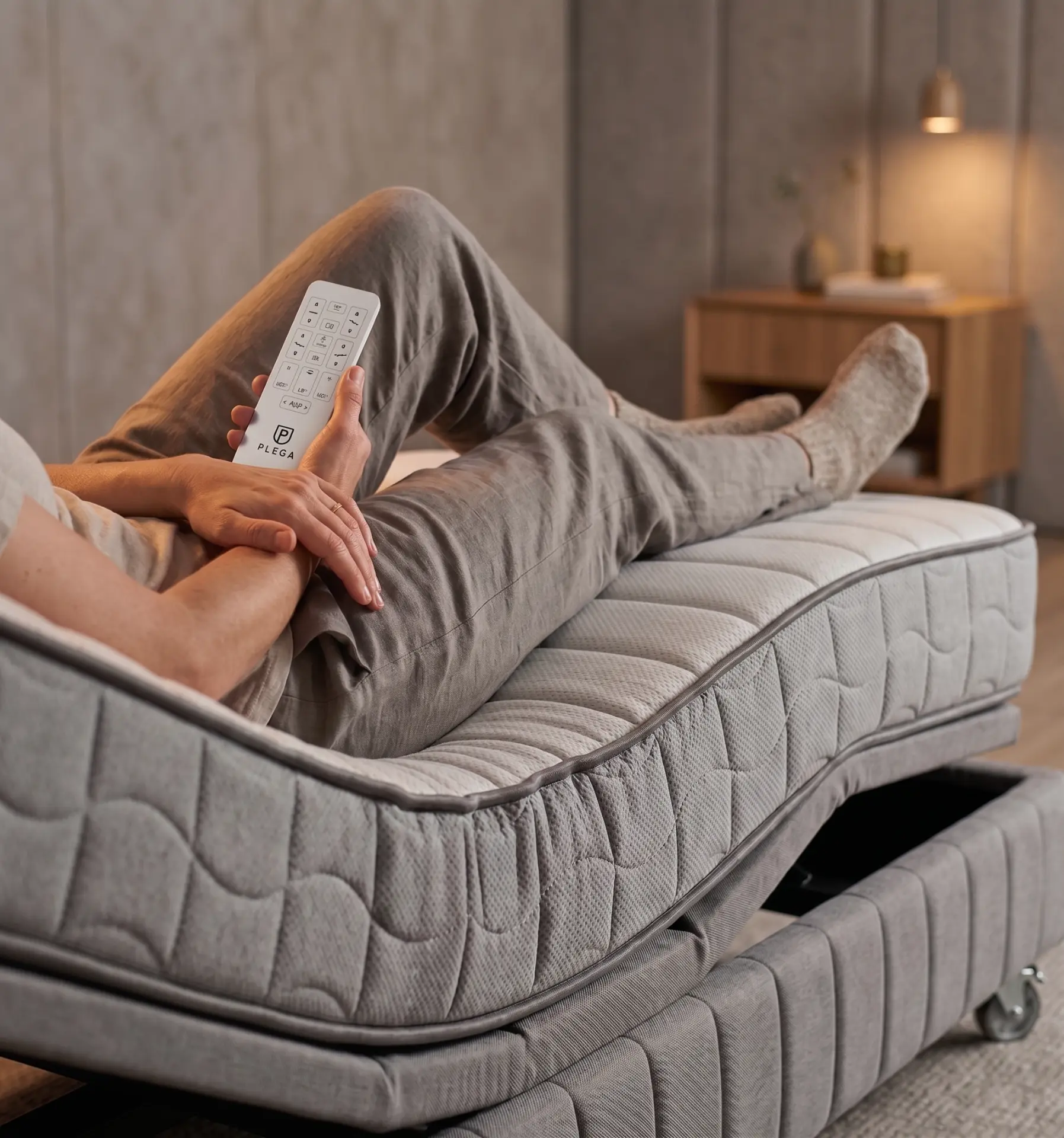 Person relaxing on the PLEGA Z-SERIES 2 with legs raised, holding the PLEGA wireless hand control