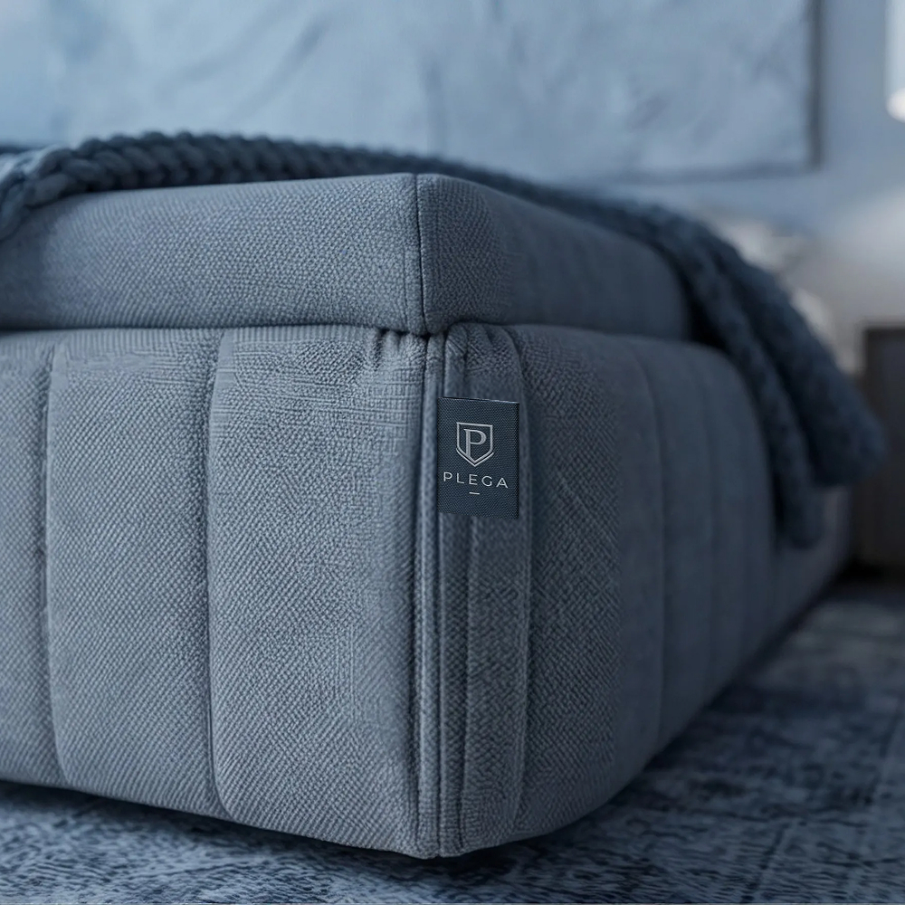 Close-up of the Z-Series 2 grey channel-stitched upholstered base with PLEGA tag